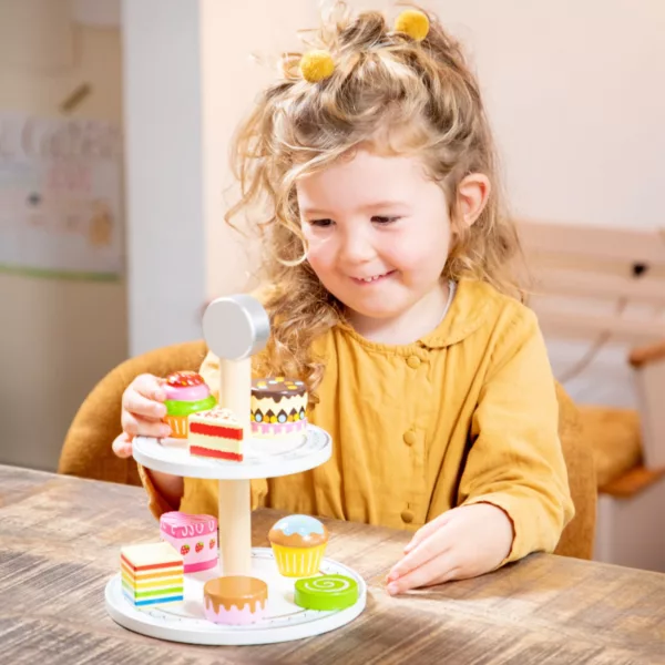 Дете подрежда дървени кексчета върху двуетажен поднос New Classic Toys за 3+