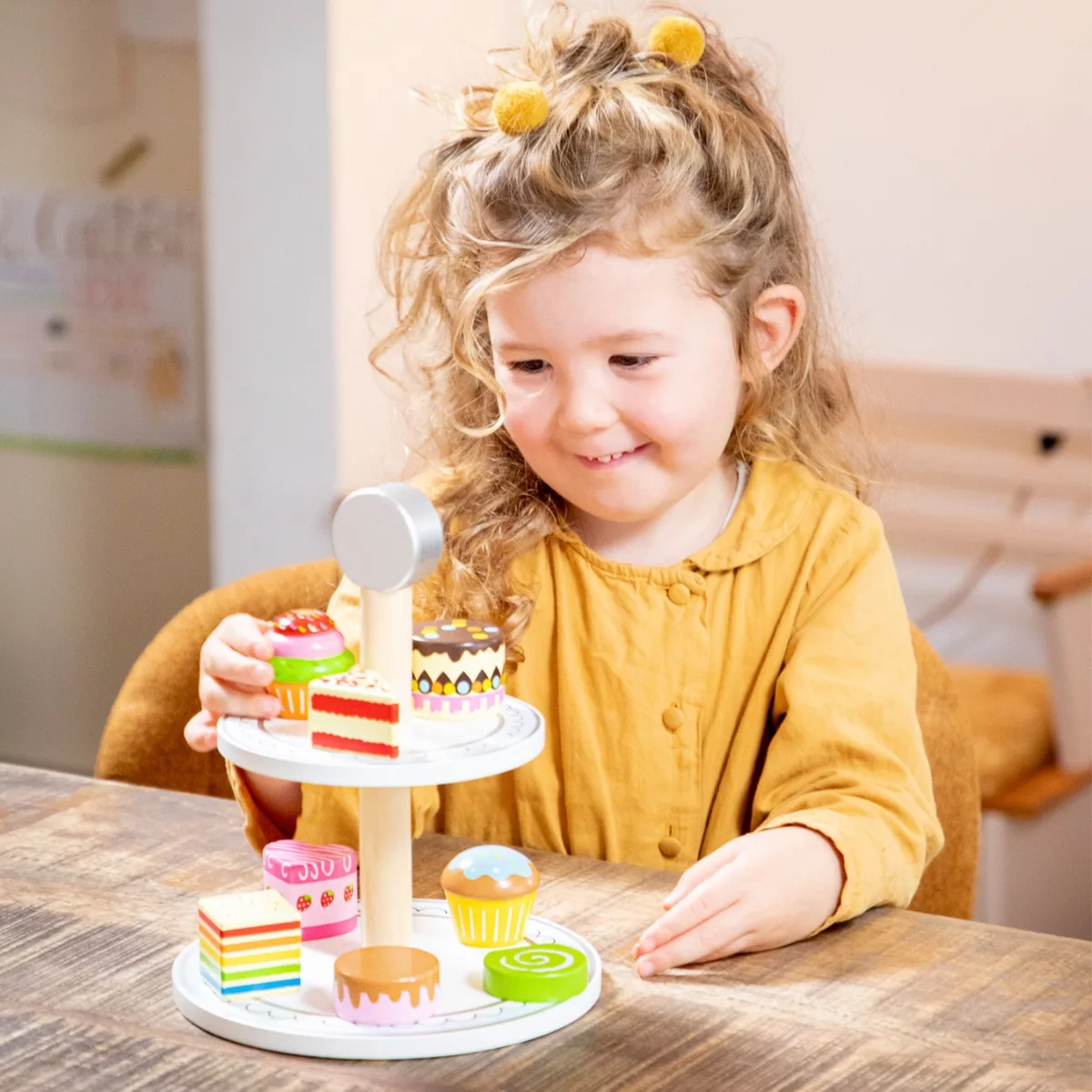 Дете подрежда дървени кексчета върху двуетажен поднос New Classic Toys за 3+