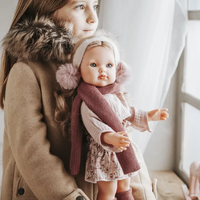 Момиче държи кукла Белла с наушници в уютна домашна обстановка