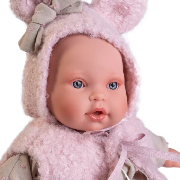 Говореща кукла бебе Кика – с пухкава жилетка, меко тяло и биберон 27 см, близък план на лицето с розова пухкава качулка с ушички и сива панделка.