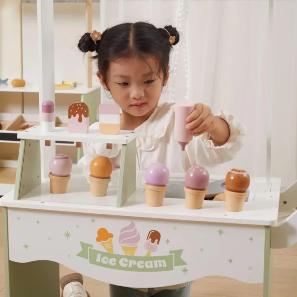 Малко момиче играе с дървен щанд за сладолед на колела Polar B - детайлен поглед към разнообразните сладоледени форми в пастелни цветове