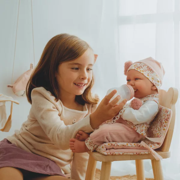 Момиченце храни с шишенце кукла бебе Карла с цветна шапка в дървен стол