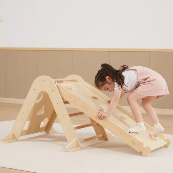 Момиче в розова рокля се катери по дървена пързалка Viga Toys - образователна играчка за развитие на координация и сила при децата