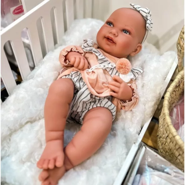 Кукла бебе Пипа с раирана лента за глава и персикова дреха на бяла постелка в креватче