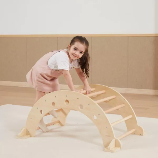 Момиче с розова рокля играе с дървена арка за катерене и люлка от Viga Toys - детска мебел за физическо развитие в естествена детска стая