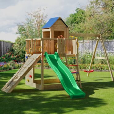 Детска площадка Fungoo TREEHOUSE – изглед отпред с пързалка, въжена рампа, кула и една люлка в зелен двор.