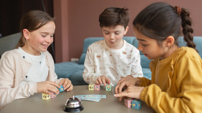 Три деца играят заедно настолна игра с цветни кубчета и карти, за концентарция, памет, сръчност