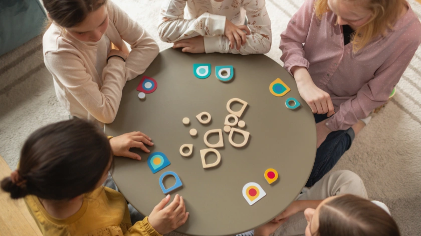 Деца играят заедно с дървени части от образователна игра на кръгла маса, те учат и развиват фината си моторика, ловкостта и паметта