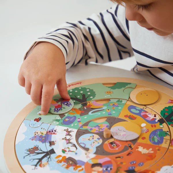 Малко дете с раирана блуза играе с образователния пъзел "Четири сезона в градината", поставяйки елемент на дървената основа.