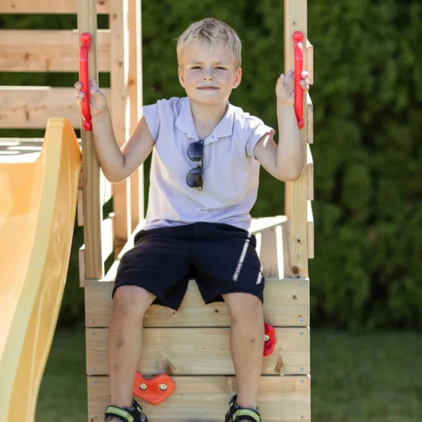 детска площадка Wendi Toys M40- дете момченце седи усмихнато върху стената за катерене на дървеният игрален комплекс