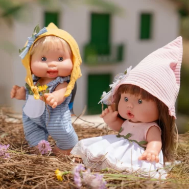 Две кукли бебета Marina & Pau със стилни летни облекла и шапки, играещи сред цветя от Bellamiestore