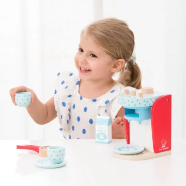 Момиче се усмихва докато играе с дървена кафе машина Bon Appetit от New Classic Toys, налична в Bellamiestore.