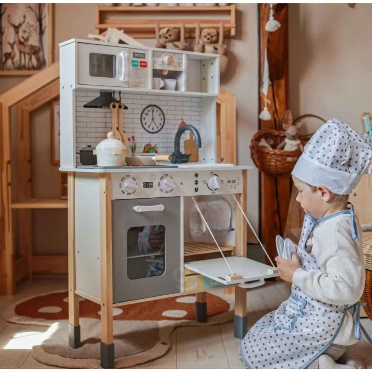 Момче с готварска престилка играе с дървена кухня Jolly Toy, отваря миялна машина, дърво и бели детайли
