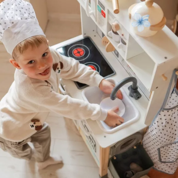 Усмихнато момче готви и мие чинии на детска дървена кухня Jolly Toy с реалистични функции