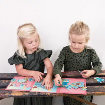 Две момичета подреждат малки картонени пъзели за деца, забавна и обучаваща игра на маса