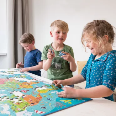 Група деца редят голям картонен пъзел карта на света, образователна игра за развитие на знания