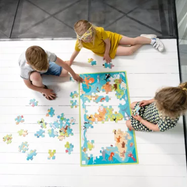 Три деца подреждат картонен пъзел с морски животни, цветна и образователна игра за малки деца