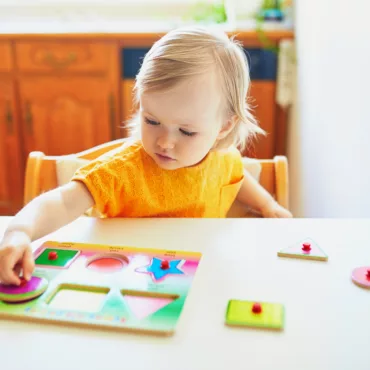 Бебе играе с дървен пъзел с дръжки, развиващ форми и цветове, безопасен за малки деца