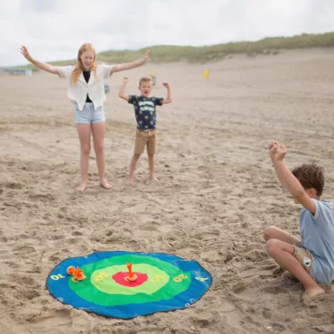 Деца на плажа играят с мишена за хвърляне на торбички, развиваща точност и концентрация