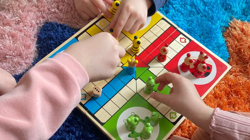 Детски ръчички играят с дървена настолна игра на цветен килим – радост, приятелство и споделена игра.