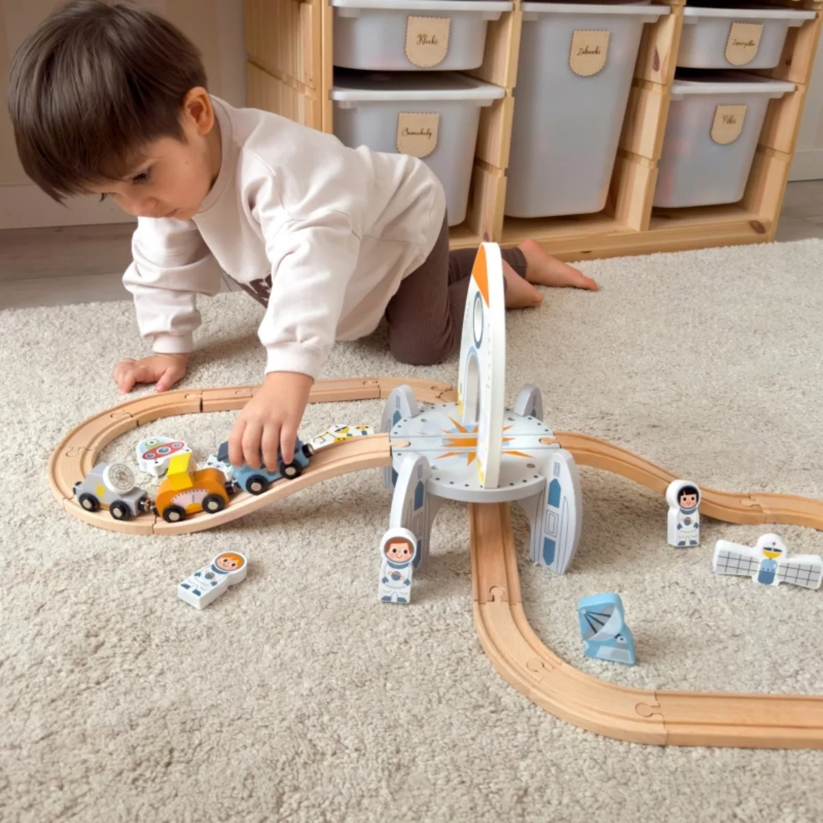 Момче играе с дървен влак с релси – Космическа станция от Tooky Toy, цветен килим, 3+ години