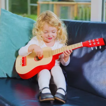 Момиче свири на класическа дървена детска китара с червен кант, подходяща за начинаещи, 3+ години