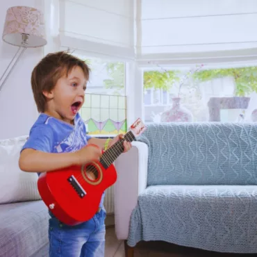 Момче свири на червена дървена китара с колан, подходяща за деца, класически струнен инструмент