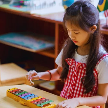 Момиче свири на цветен детски ксилофон, метални пластини, дървена основа, подходящ за училище.