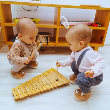 Два бебока свирят на голям дървен ксилофон, естествен материал, подходящ за ранно музикално развитие.