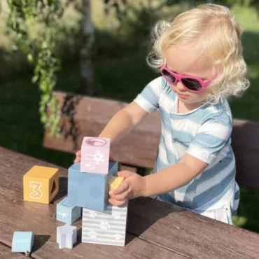 Момиче с руса коса реди дървени блокчета, образователна игра за бебета, рингове и сортери, жълто и синьо
