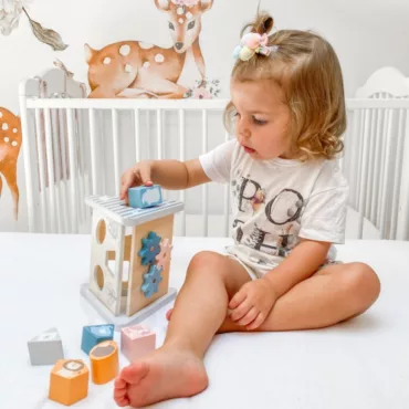 Момиче седи и играе с дървен сортер за форми, бебешка образователна играчка, пастелни блокчета
