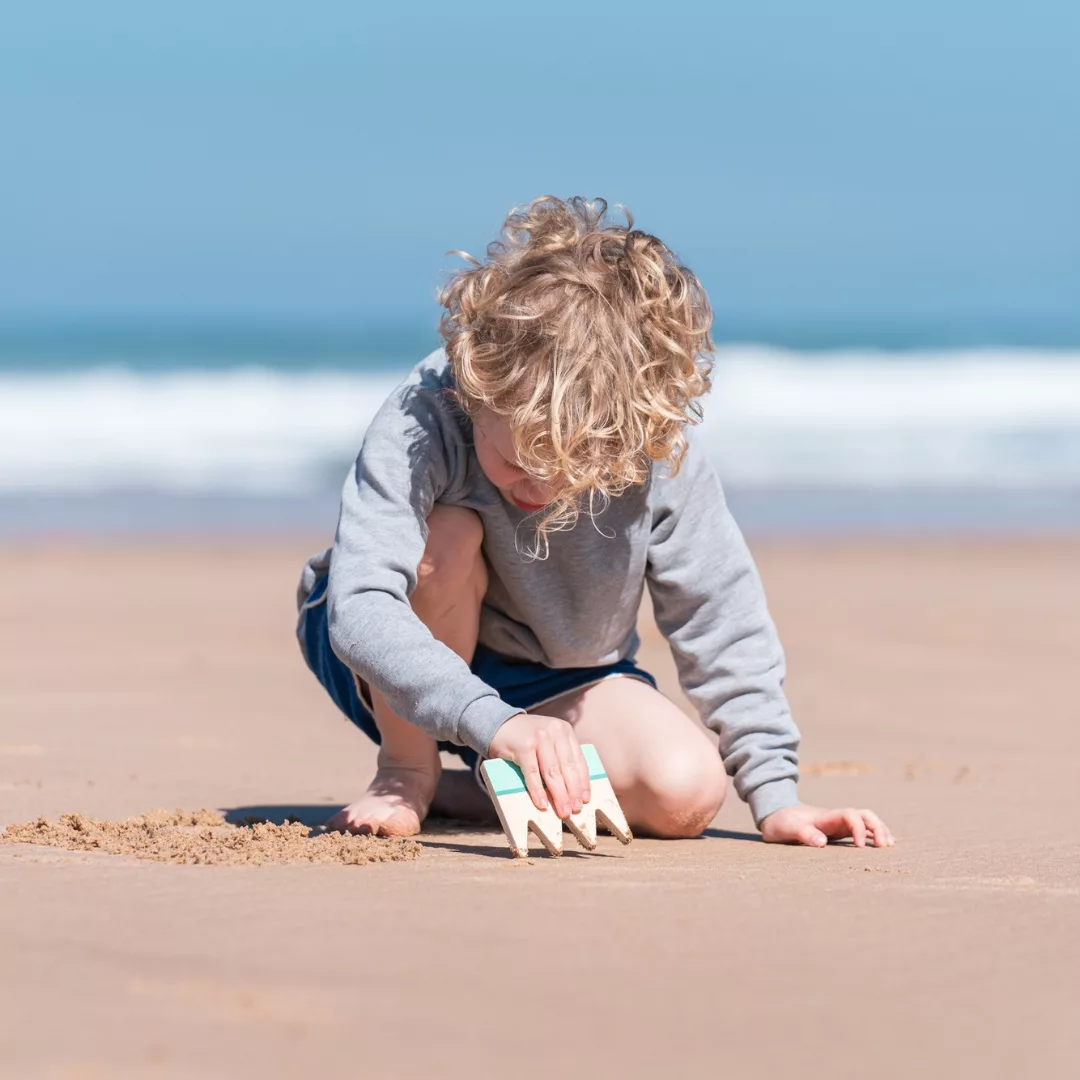 Дете рисува с дървен комплект за рисуване в пясък от BS Toys на плажа