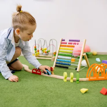 Дете играе с дървен влак и образователни Монтесори играчки на пода