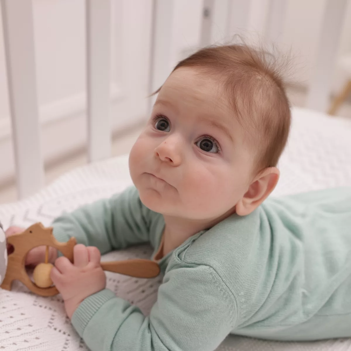 Бебе играе с дървена дрънкалка от естествено дърво – безопасна играчка за количка