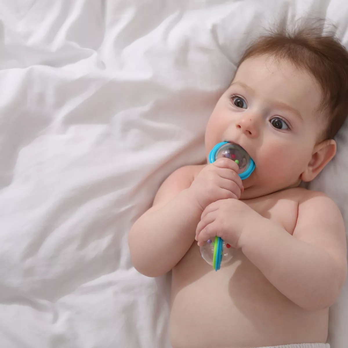 Бебе държи прозрачна бебешка дрънкалка с цветни топчета – играчка за количка