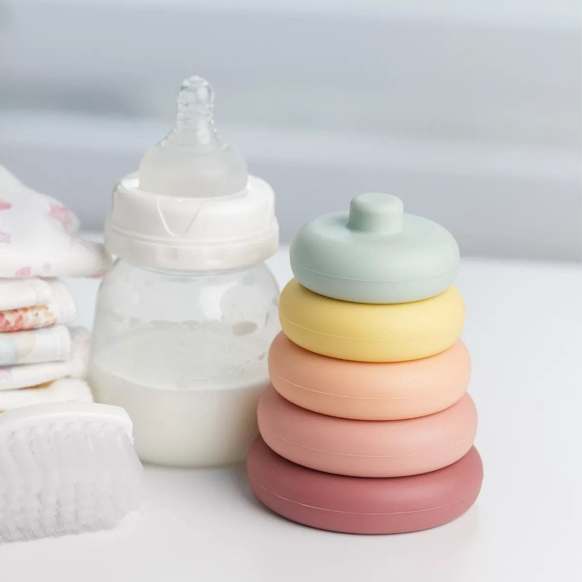 Рингове за подреждане пастелни цветове и бебешка бутилка върху бяла маса