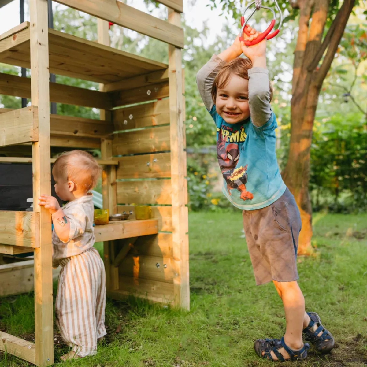 Деца играят под дървена площадка с кухня и катерушка на открито