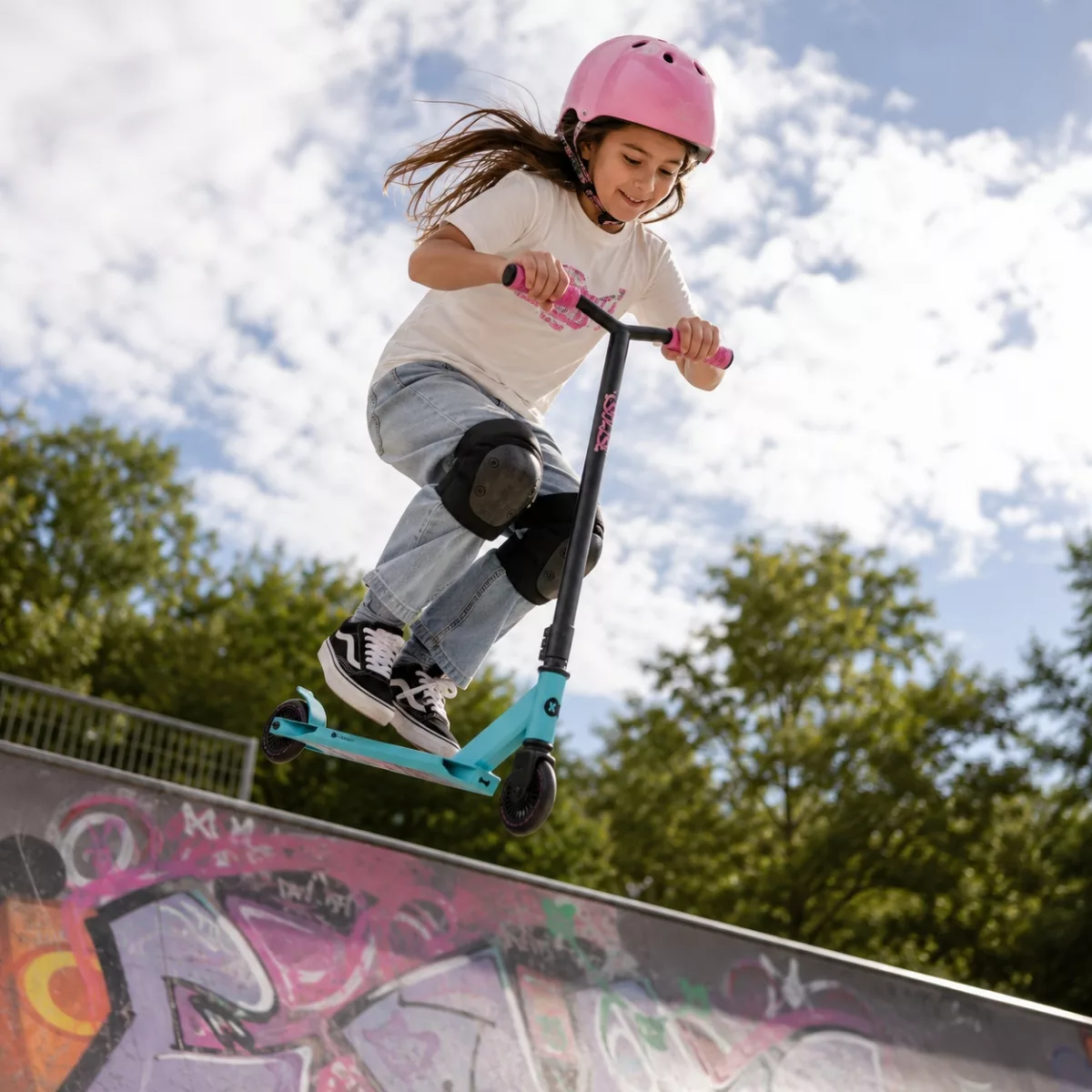 Момиче прави скок със спортна тротинетка Kinderkraft SOLIS Pink на скейт рампа