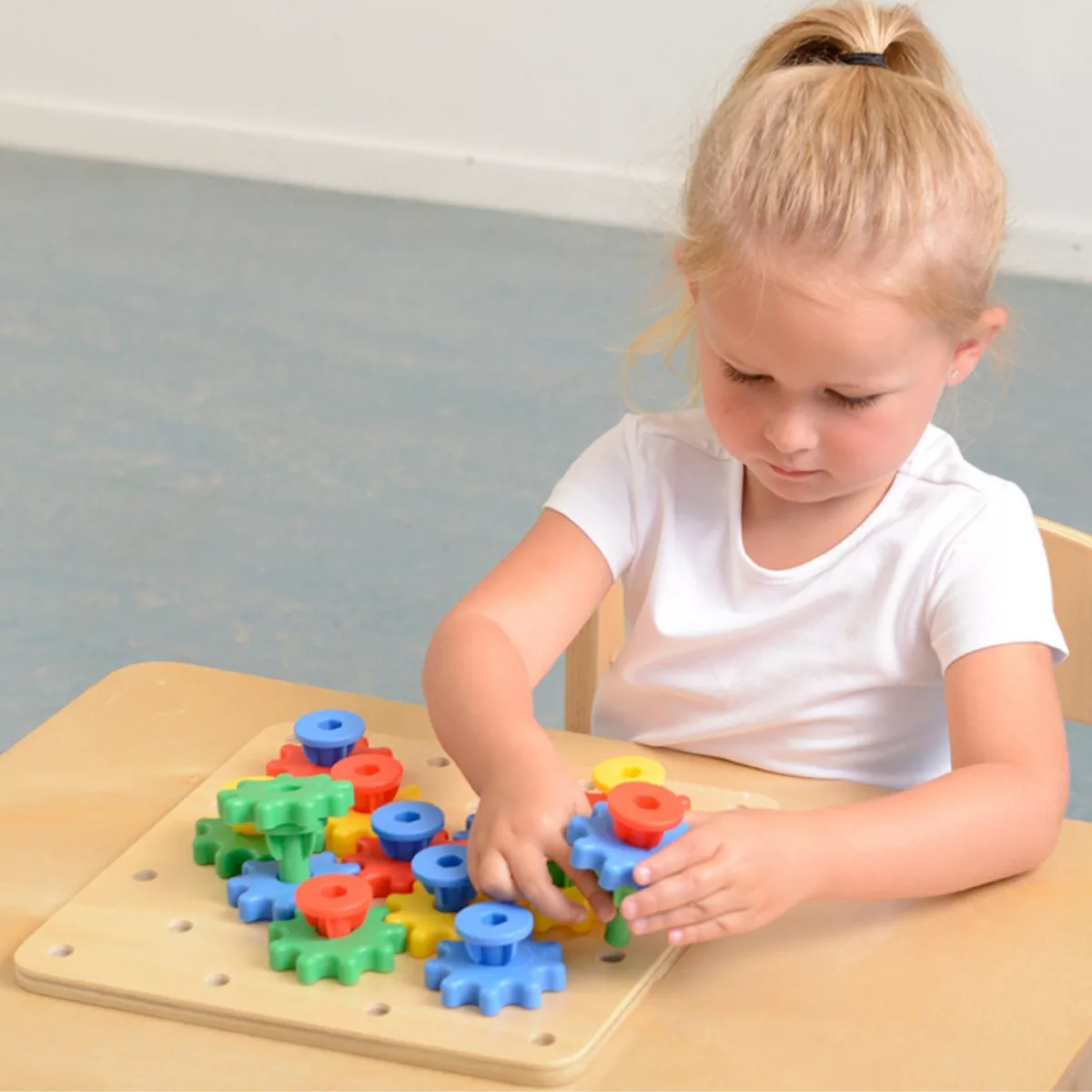 Момиче закрепва синьо зъбно колело върху дъска Masterkidz с механизъм на няколко нива.