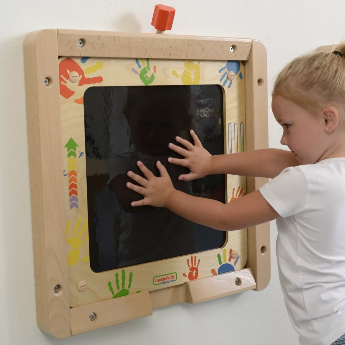 Дете притиска длани към черната повърхност на термочувствителна дъска Masterkidz с цветно украсена дървена рамка.
